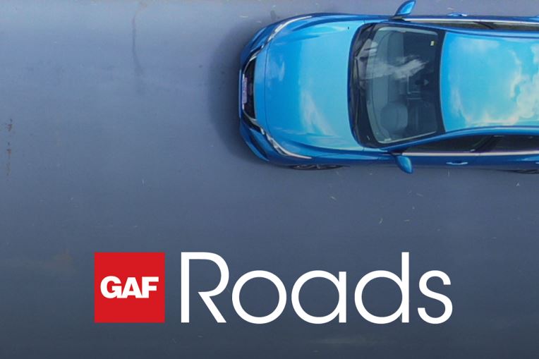 Blue car driving on street with new GAF Roads roadway maintenance