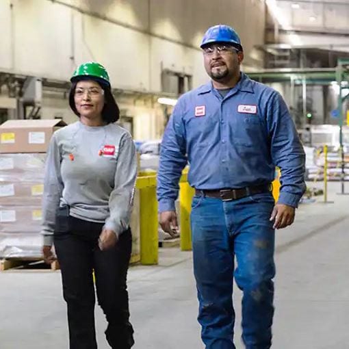 Female and male GAF employees walking in roofing manufacturing plant