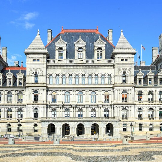 A front-facing view of the New York State Capitol building; a grand, multi-story historic building with ornate architectural details.