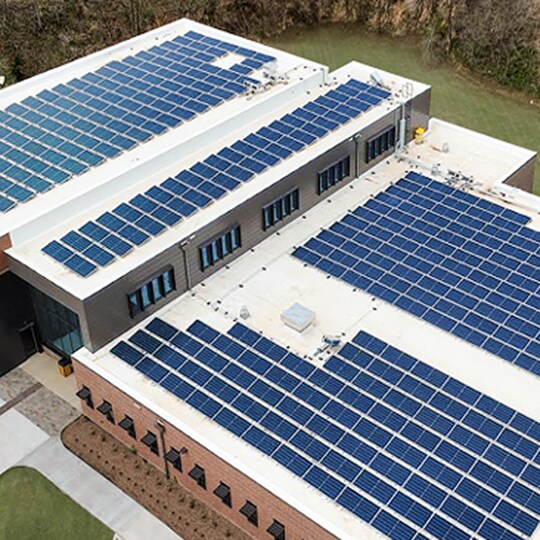 A high-angle shot of a commercial building rooftop covered in multiple rows of blue solar panels for renewable energy generation.
