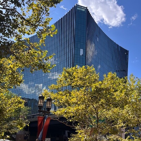 10 World Trade building under a blue sky is framed by lush green trees. 