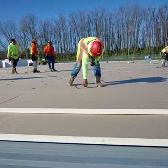 A GAF certified contractor preparing a flat roof deck for insulation installation, with team members in the background.