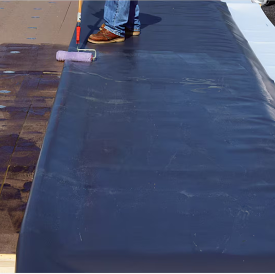 A GAF certified contractor applying single-ply roofing adhesive on a commercial roof deck.