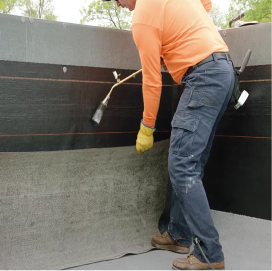 A GAF certified contractor torch-applying an APP modified bitumen membrane onto a wall detail.