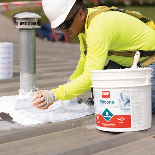 Roofing contractor treating penetrations with GAF Silicone Mastic before coating 