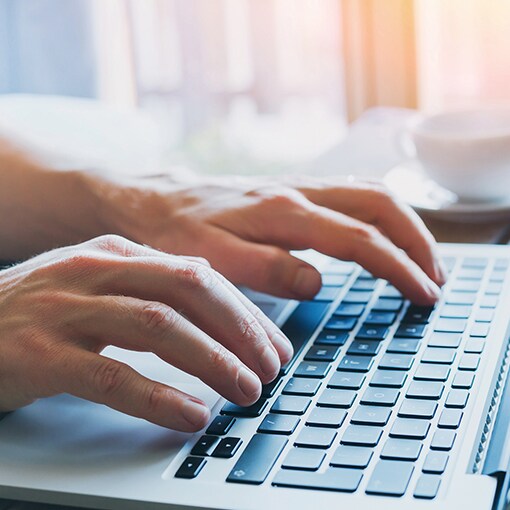 A close-up of a person's hands typing on a laptop keyboard.
