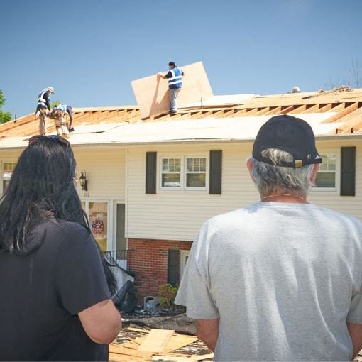 Man and woman watching GAF contractors working on a new roof.