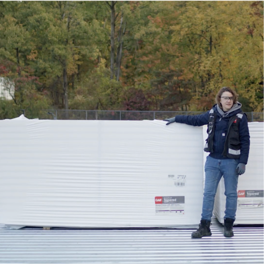 A GAF certified contractor standing beside a large bundle of 4' x 8' polyiso insulation boards on site.