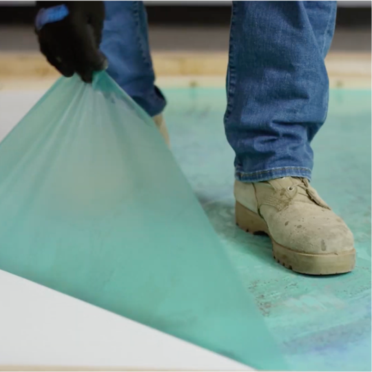 A GAF certified contractor peeling protective EverGuard MembraneShield film off a white roof membrane.
