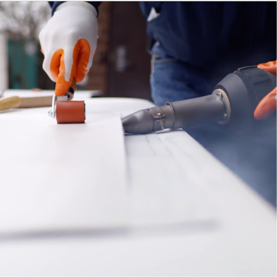 Close-up of a GAF certified contractor adhering EverGuard PVC membrane using a hand roller and hot-air welder.