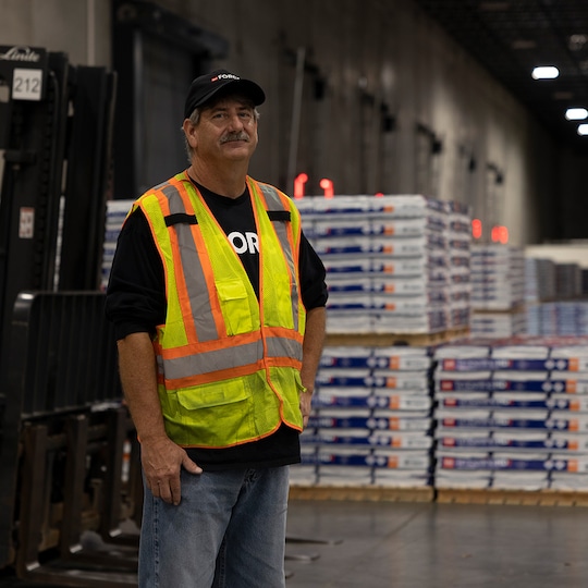 GAF roofing employee in front of stacks of shingles in packages