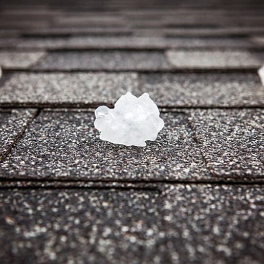 An asphalt shingle roof with hail balls laying on it.