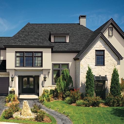 A beige home with dark gray Camelot® II roof shingles by GAF that meet the criteria of the FORTIFIED™ Program.