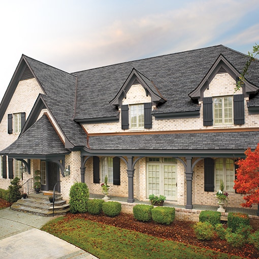 A light brick house with gray Woodland® roof shingles from GAF that meet the criteria of the FORTIFIED™ Program.