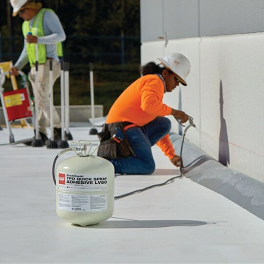 A roofer installs GAF’s TPO Quick Spray Adhesive on a flat roof