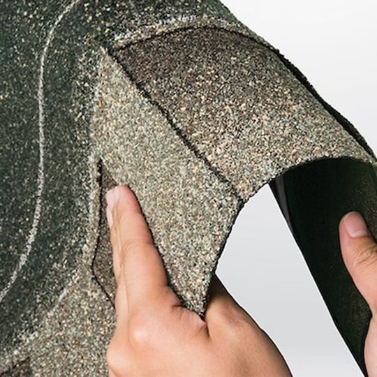 Hands bending a strip of shingles produced by GAF, showing how flexible and durable it is