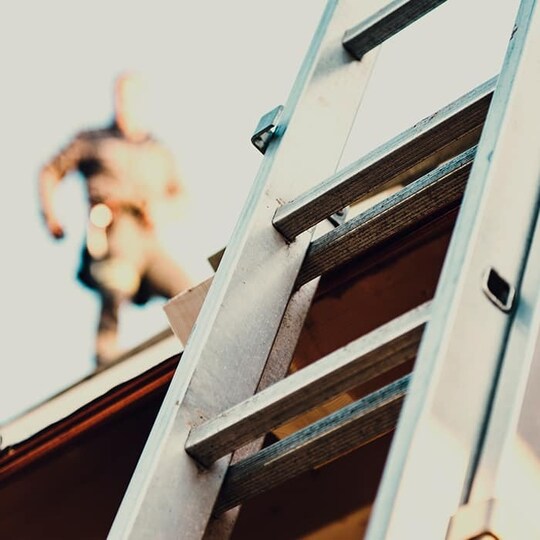 ladder on a roof with a roofer in the background
