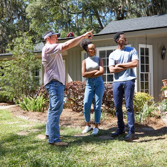 Roofing contractor with the  National Circle™ designation from GAF pointing out information to two homeowners outside their home.