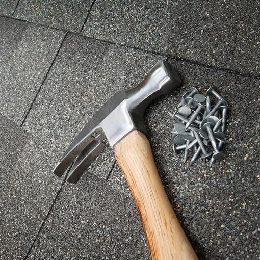 Nail and hammer on top of asphalt roof shingles