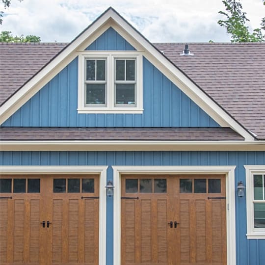 A large vintage retro detached two car cape cod blue style garage, with grey shingled roof, windows,