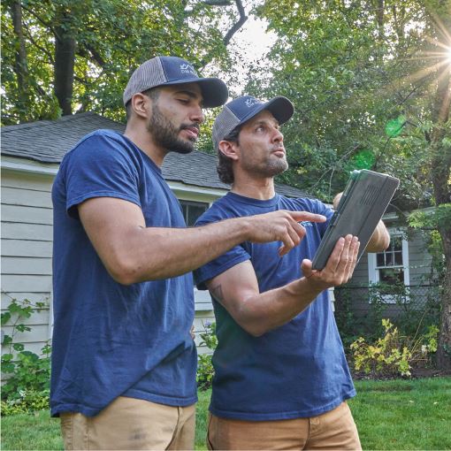 Two GAF contractors review documents on a tablet on a job site.