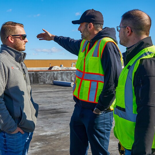 Three GAF certified professionals standing on a commercial roof discussing the project.