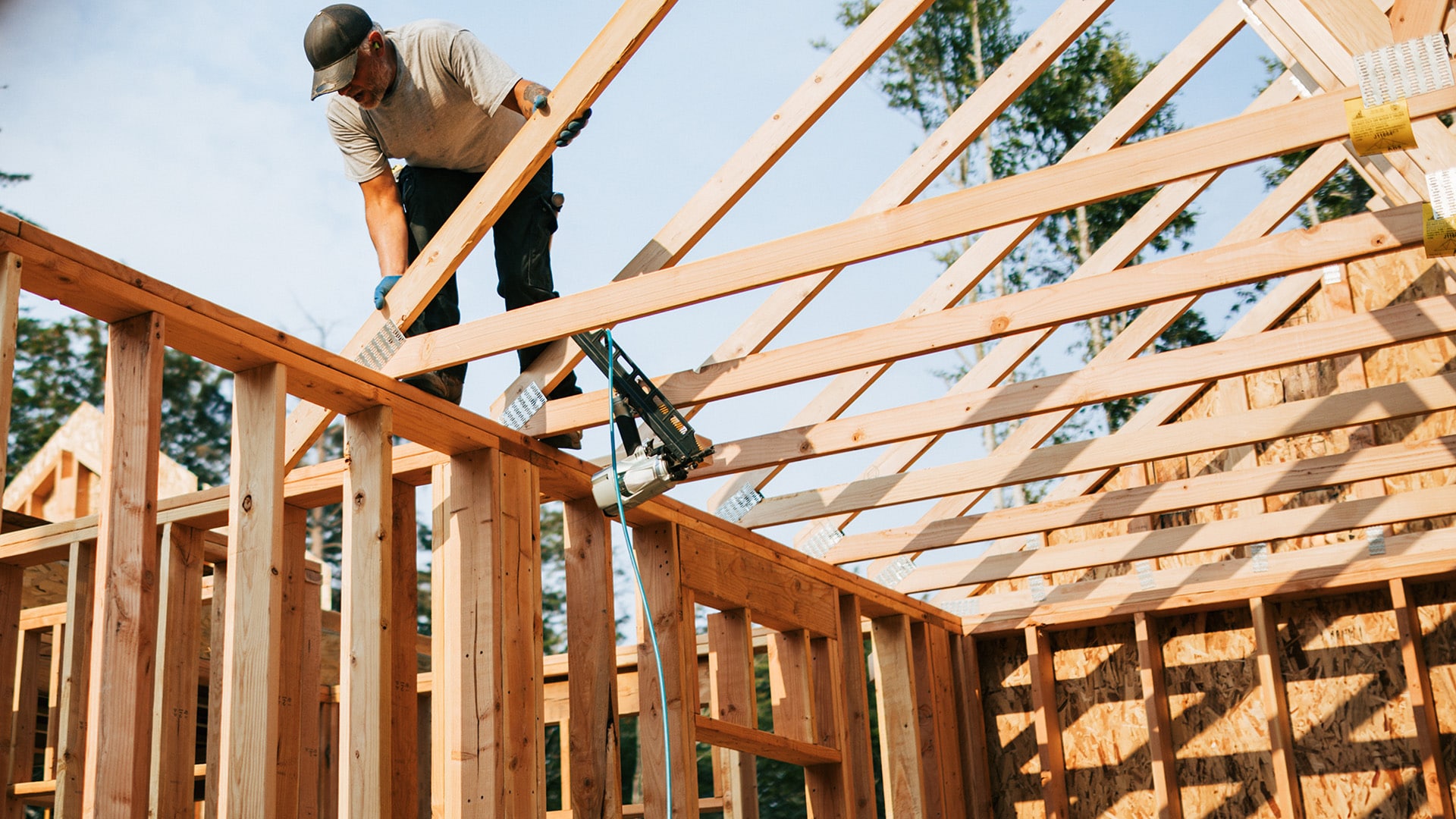 A contractor working on a wooden roof frame on a partially build house.