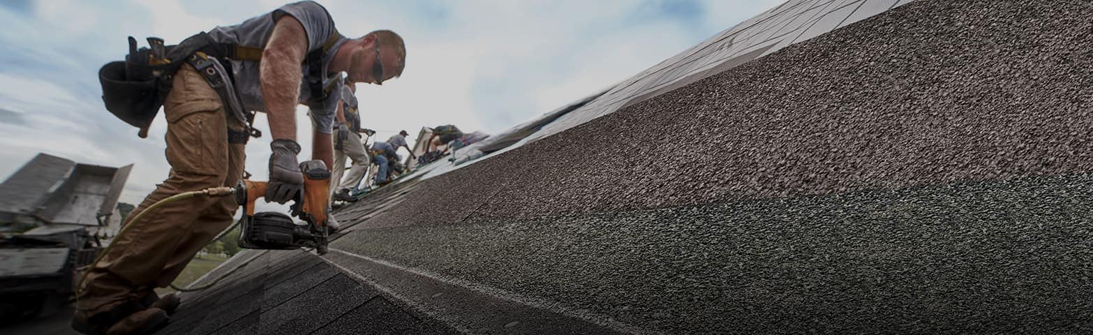 Roofer using a nail gun to secure new GAF shingles on a pitched roof