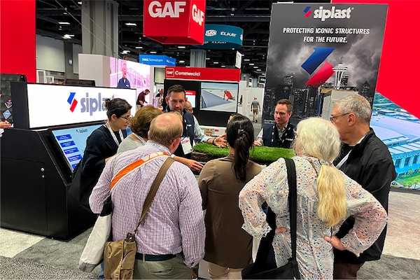 A group of people watching a demonstration at the Siplast booth. 