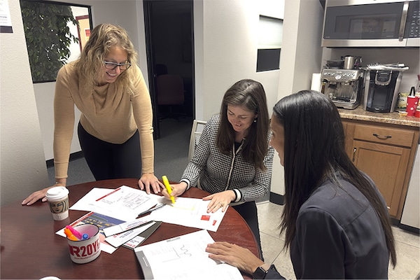 Three members of the GAF Building & Roofing Science team collaborating over project documents at a table in an office setting.