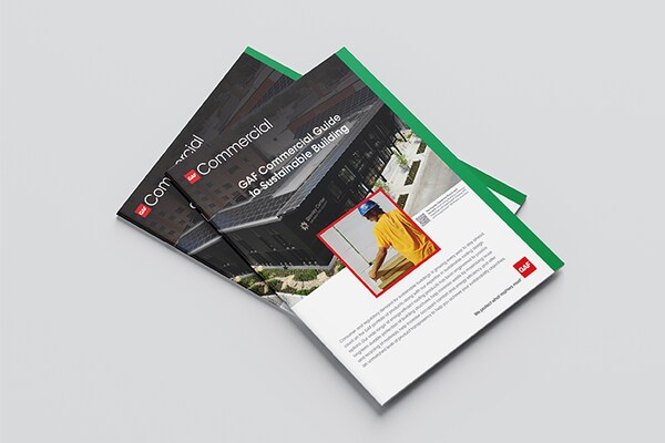 The "GAF Commercial Guide to Sustainable Building" brochure rests on a white surface, featuring a cover photo of a modern building and a GAF Commercial Certified contractor at work.