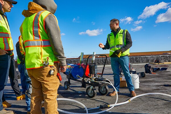 Two GAF certified contractors in winter safety gear installing a single-ply membrane in cold weather conditions.