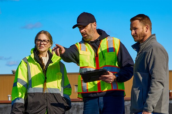 A GAF Territory Manager in a high-visibility vest consulting with two GAF certified contractors on a commercial job site.