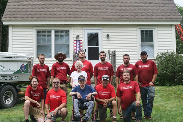 Volunteers in the Roofs for Heros Program  pose with a veteran and his wife in front of a house.