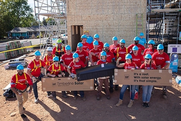 A group of GAF volunteers in blue hard hats and red shirts posing for a photo at a job site.