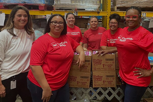 Six GAF employees wearing red shirts with a "Community Matters" logo stand smiling together in a warehouse where they are volunteering their time.