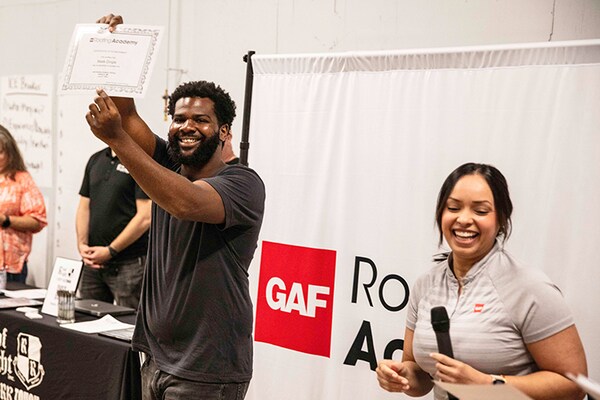 Student holding a certificate at a GAF Roofing Academy skilled trades training event.