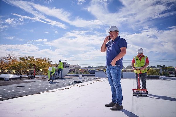 A commercial property owner inspecting a roof project while GAF certified contractors install a white membrane roof in the background.