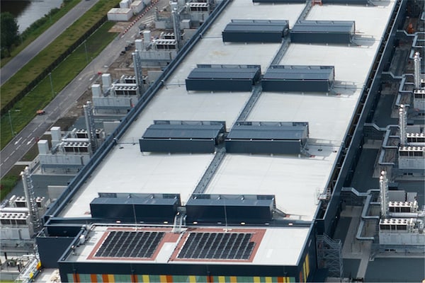 An aerial view of a large data center complex featuring two rectangular buildings with flat roofs covered in mechanical equipment and solar panels.