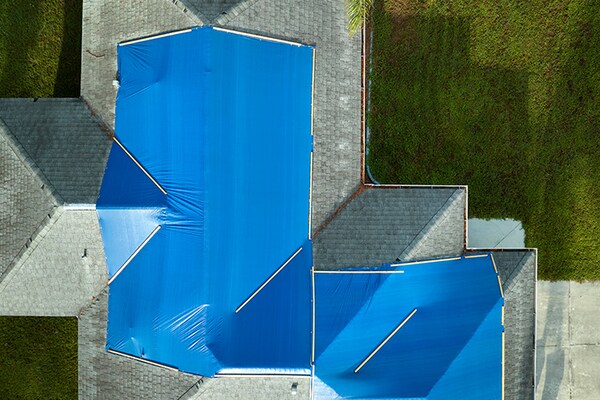 A bird’s eye view of a roof that’s partially covered with tarps to protect it from further storm damage. 