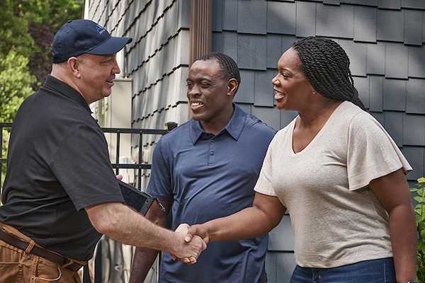 A contractor speaking to a homeowner couple about a roofing project while they stand outside of their house. 