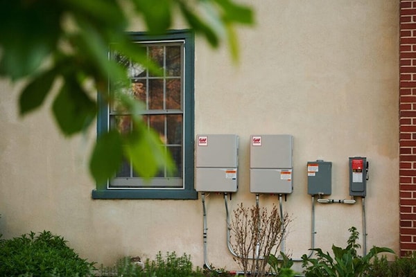 Electrical boxes on the exterior back wall of a house with GAF Energy stickers. 