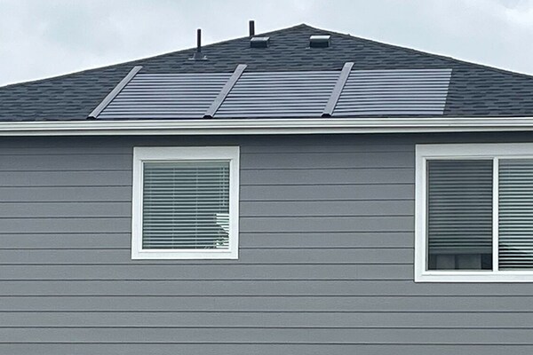 A residential house with gray siding and a dark gray shingled roof featuring the Timberline Solar Roofing System. 