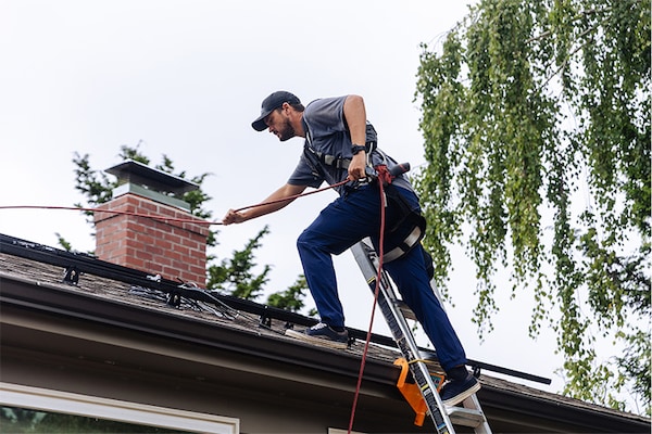A GAF certified contractor wears a safety harness while stepping onto a shingle roof to do a roof repair. 