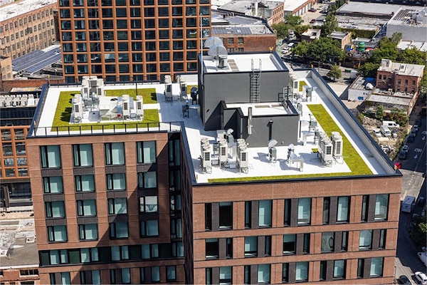 Aerial view of a modern urban commercial building featuring a white membrane roof and green rooftop garden areas.
