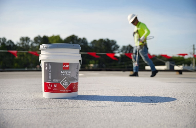 A contractor applying GAF acrylic top coat on a flat roof.