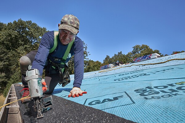 Roofing contractor using a pneumatic nail gun to install GAF starter strip shingles along roof eaves.