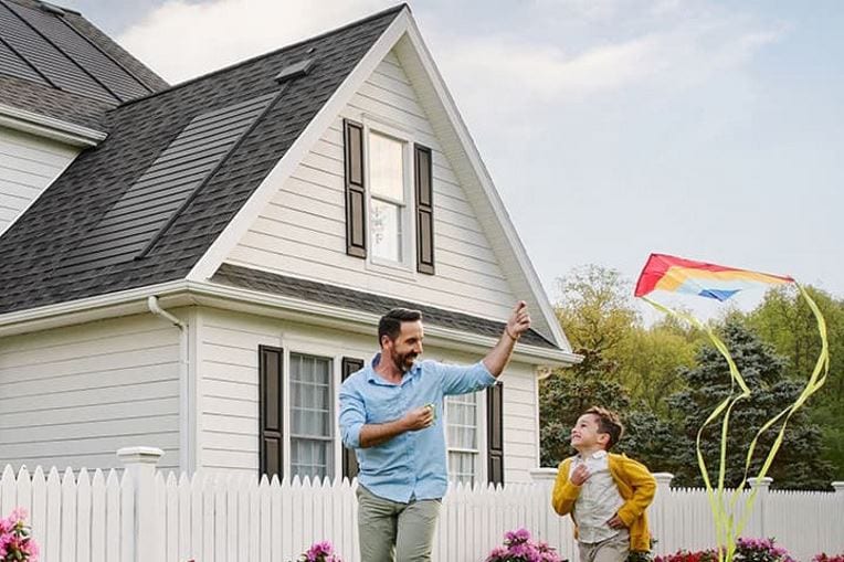 Father and son flying kite outside home with a GAF Energy solar roof