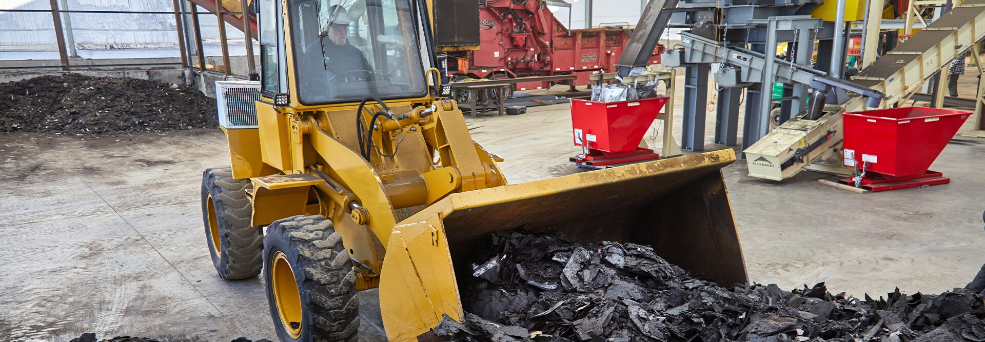 A front-end loader scoops up torn, old asphalt shingles to be processed as part of the GAF RoofCycle program.