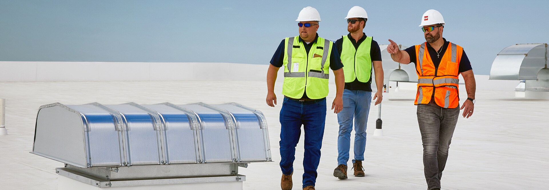 Three GAF Commercial Certified contractors in safety vests and hard hats walking across a white TPO rooftop.